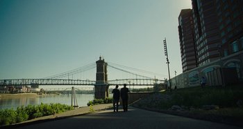 Movie still from “The Killing of a Sacred Deer” (2017), directed by Yorgos Lanthimos – Two people walking on a sidewalk near a bridge; Extreme Wide shot, Over the shoulder angle