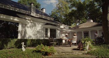 Movie still from “The Killing of a Sacred Deer” (2017), directed by Yorgos Lanthimos – Two people sitting at an outdoor table outside a house; Extreme Wide shot, High angle