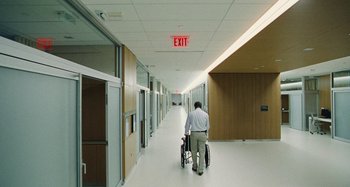 Movie still from “The Killing of a Sacred Deer” (2017), directed by Yorgos Lanthimos – A man pushing a wheelchair down a long hallway; Wide shot, High angle