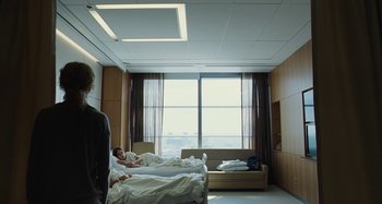 Movie still from “The Killing of a Sacred Deer” (2017), directed by Yorgos Lanthimos – Two people are lying in a bed in a hospital room; Wide shot, Over the shoulder angle