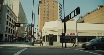 Movie still from “The Killing of a Sacred Deer” (2017), directed by Yorgos Lanthimos – Two people cross the street in front of a building; Extreme Wide shot, High angle
