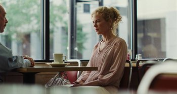 Movie still from “The Killing of a Sacred Deer” (2017), directed by Yorgos Lanthimos – A woman sitting at a table with a cup of coffee in front of a window; Medium shot, Over the shoulder angle