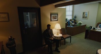 Movie still from “The Killing of a Sacred Deer” (2017), directed by Yorgos Lanthimos – A man in a suit sitting on a chair next to a lamp; Wide shot, High angle