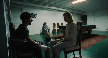 Movie still from “The Killing of a Sacred Deer” (2017), directed by Yorgos Lanthimos – A woman sitting on a chair in front of two men; Wide shot, Over the shoulder angle