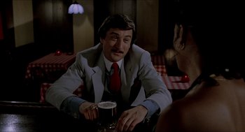Movie still from “The King of Comedy” (1982), directed by Martin Scorsese – A man sitting at a table with a glass of beer in front of him; Medium shot, Over the shoulder angle