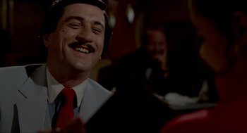 Movie still from “The King of Comedy” (1982), directed by Martin Scorsese – A man in a suit and red tie is smiling; Close Up shot, Over the shoulder angle
