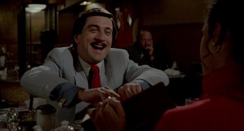 Movie still from “The King of Comedy” (1982), directed by Martin Scorsese – A man in a suit sitting at a table; Close Up shot, Over the shoulder angle