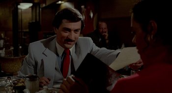Movie still from “The King of Comedy” (1982), directed by Martin Scorsese – A man sitting at a table in a restaurant; Close Up shot, Over the shoulder angle
