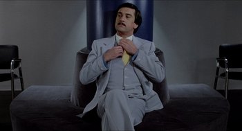Movie still from “The King of Comedy” (1982), directed by Martin Scorsese – A man sitting in a chair with a suit and a tie; Medium shot, Low angle