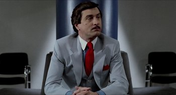 Movie still from “The King of Comedy” (1982), directed by Martin Scorsese – A man in a suit and red tie sitting in a chair; Close Up shot, Low angle