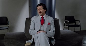 Movie still from “The King of Comedy” (1982), directed by Martin Scorsese – A man sitting on a chair wearing a suit and tie; Medium shot, Over the shoulder angle