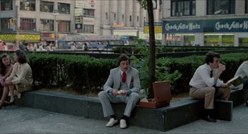 Movie still from “The King of Comedy” (1982), directed by Martin Scorsese – A man sitting on a bench in a suit and red tie; Wide shot, High angle