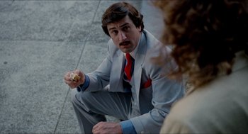 Movie still from “The King of Comedy” (1982), directed by Martin Scorsese – A man sitting on the ground eating a donut; Close Up shot, Over the shoulder angle