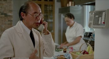 Movie still from “The King of Comedy” (1982), directed by Martin Scorsese – An older man talking on the phone while a woman prepares a meal; Medium shot, Over the shoulder angle