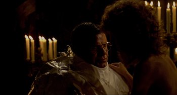 Movie still from “The King of Comedy” (1982), directed by Martin Scorsese – A man wearing a priest's outfit and glasses is sitting in front of candles; Close Up shot, Over the shoulder angle
