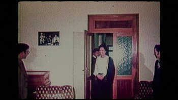 Movie still from “The Kingmaker” (2019), directed by Lauren Greenfield – A woman standing in a doorway with a man standing next to it; Wide shot, Over the shoulder angle