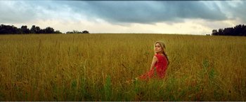 Movie still from “The Kings of Summer” (2013), directed by Jordan Vogt-Roberts – A woman in a red dress sitting in a field; Wide shot, Low angle