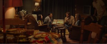 Movie still from “The Kings of Summer” (2013), directed by Jordan Vogt-Roberts – A group of people sitting around a living room table; Wide shot, Over the shoulder angle