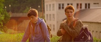 Movie still from “The Kings of Summer” (2013), directed by Jordan Vogt-Roberts – Two young men walking down a sidewalk near a building; Medium shot, Low angle
