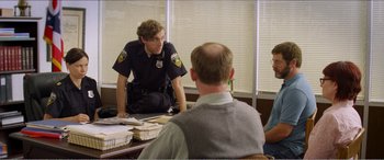 Movie still from “The Kings of Summer” (2013), directed by Jordan Vogt-Roberts – A police officer sitting at a table talking to two men; Medium shot, Over the shoulder angle