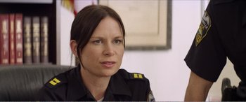 Movie still from “The Kings of Summer” (2013), directed by Jordan Vogt-Roberts – A woman in a police uniform sitting in front of a wall; Close Up shot, Over the shoulder angle