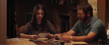 Movie still from “The Kings of Summer” (2013), directed by Jordan Vogt-Roberts – Two people sitting at a dinner table looking at a piece of paper; Medium shot, Over the shoulder angle