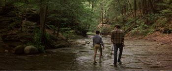 Movie still from “The Kings of Summer” (2013), directed by Jordan Vogt-Roberts – Two people standing in a stream in a wooded area; Wide shot, Over the shoulder angle