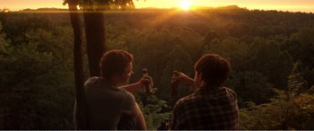 Movie still from “The Kings of Summer” (2013), directed by Jordan Vogt-Roberts – Two men are drinking beers at sunset in the woods; Wide shot, Over the shoulder angle