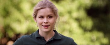 Movie still from “The Kings of Summer” (2013), directed by Jordan Vogt-Roberts – A young woman is smiling for the camera outside; Close Up shot, Over the shoulder angle