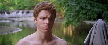 Movie still from “The Kings of Summer” (2013), directed by Jordan Vogt-Roberts – A man with a beard is standing in front of a body of water; Close Up shot, Over the shoulder angle