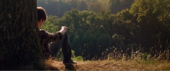Movie still from “The Kings of Summer” (2013), directed by Jordan Vogt-Roberts – A person sitting on the ground in the grass; Wide shot, High angle