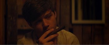 Movie still from “The Kings of Summer” (2013), directed by Jordan Vogt-Roberts – A young man is smoking a cigar in a room; Close Up shot, Over the shoulder angle