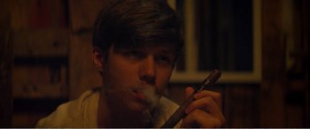 Movie still from “The Kings of Summer” (2013), directed by Jordan Vogt-Roberts – A young man smoking a cigar while sitting in a chair; Close Up shot, Low angle