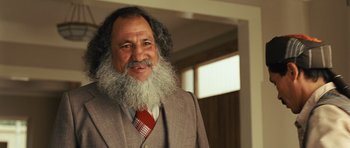Movie still from “The Kite Runner” (2007), directed by Marc Forster – A man with a beard and a suit and tie smiling; Close Up shot, Over the shoulder angle