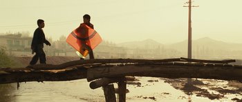 Movie still from “The Kite Runner” (2007), directed by Marc Forster – A person standing on a bridge with an orange kite; Wide shot, Low angle