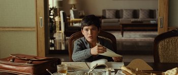 Movie still from “The Kite Runner” (2007), directed by Marc Forster – A boy sitting at a dining room table holding a paper plane; Medium shot, High angle