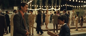 Movie still from “The Kite Runner” (2007), directed by Marc Forster – A group of people standing in a room with lights in the background; Medium shot, Over the shoulder angle