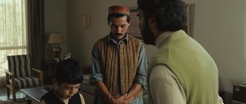 Movie still from “The Kite Runner” (2007), directed by Marc Forster – A man wearing a hat is standing in front of two other men; Medium shot, Over the shoulder angle
