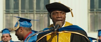 Movie still from “The Kite Runner” (2007), directed by Marc Forster – A man wearing a graduation cap and gown while speaking into a microphone; Close Up shot, Low angle