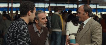 Movie still from “The Kite Runner” (2007), directed by Marc Forster – A man in a brown vest is talking to a man in a brown vest is holding a cup; Medium shot, Over the shoulder angle