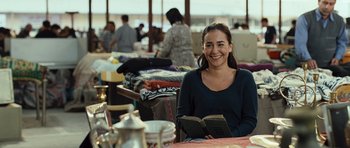 Movie still from “The Kite Runner” (2007), directed by Marc Forster – A woman sitting at a table holding an open book; Medium shot, Over the shoulder angle