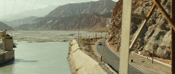 Movie still from “The Kite Runner” (2007), directed by Marc Forster – A car driving down a road next to a body of water; Extreme Wide shot, High angle