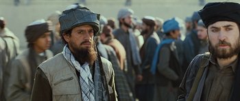 Movie still from “The Kite Runner” (2007), directed by Marc Forster – A man with a long beard wearing a hat and a tie; Medium shot, Over the shoulder angle