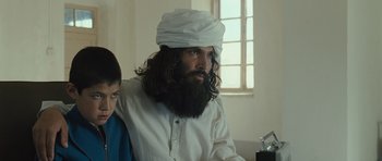 Movie still from “The Kite Runner” (2007), directed by Marc Forster – A man with long hair and a beard wearing a white turban; Medium shot, Over the shoulder angle