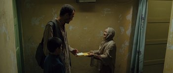 Movie still from “The Kite Runner” (2007), directed by Marc Forster – An older woman handing a letter to an older man while a young boy looks on; Medium shot, Low angle
