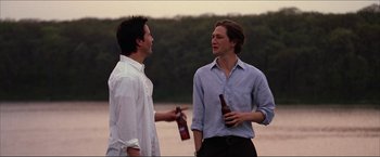 Movie still from “The Lake House” (2006), directed by Alejandro Agresti – Two young men standing next to each other holding beers; Medium shot, Over the shoulder angle