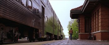 Movie still from “The Lake House” (2006), directed by Alejandro Agresti – A man walking down the street next to a green train; Extreme Wide shot, Low angle