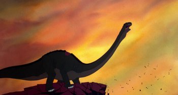 Movie still from “The Land Before Time” (1988), directed by Don Bluth – An illustration of a dinosaur standing on top of a hill; Wide shot, Low angle