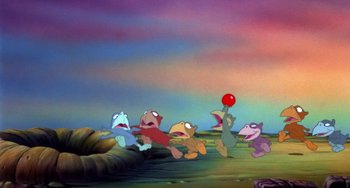 Movie still from “The Land Before Time” (1988), directed by Don Bluth – A group of cartoon characters playing with a red ball; Wide shot, High angle