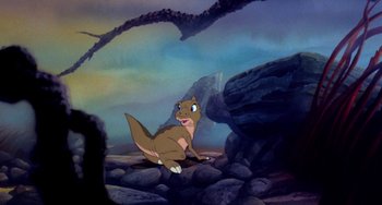 Movie still from “The Land Before Time” (1988), directed by Don Bluth – A brown and white animal sitting on top of a rock pile; Wide shot, High angle